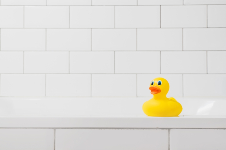 Toy yellow duck in the bathroom on a light brick background